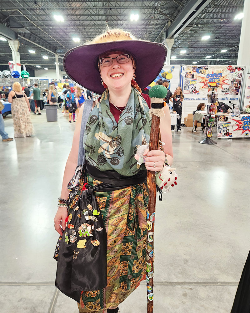 smiling person at Motor City Comic Con with cactus puff plushie on their walking stick